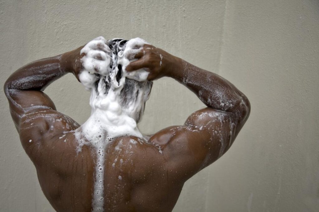 A black man washing his hair with the best shampoo in a bathroom